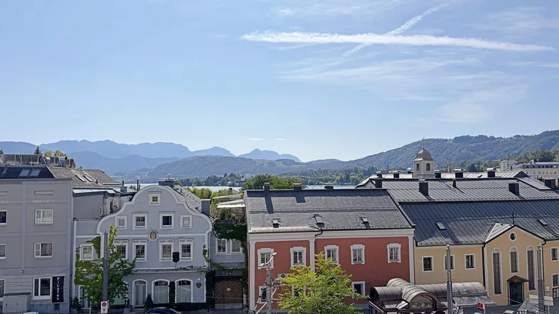 Blick über eine charmante Stadt mit traditionellen Gebäuden, einem See und majestätischen Bergen im Hintergrund.