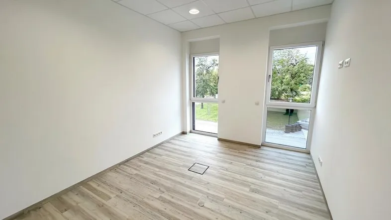 Heller, leerer Raum mit modernem Bodenbelag und großen Fenstern mit Blick ins Grüne.