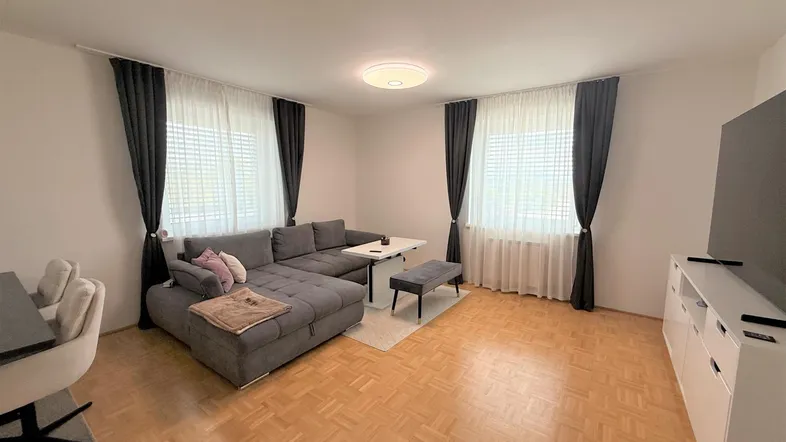 Helles Wohnzimmer mit großem Ecksofa, Parkettboden und dunklen Vorhängen, ideal zum Entspannen.