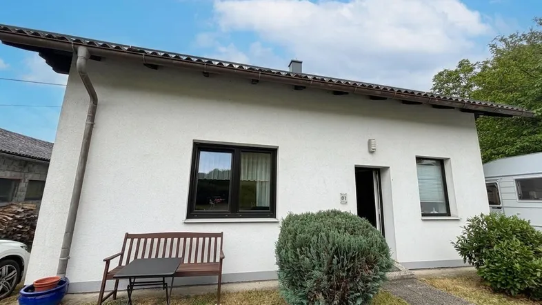 Modernes Einfamilienhaus mit weißer Fassade, kleinem Vorgarten und Sitzbank.