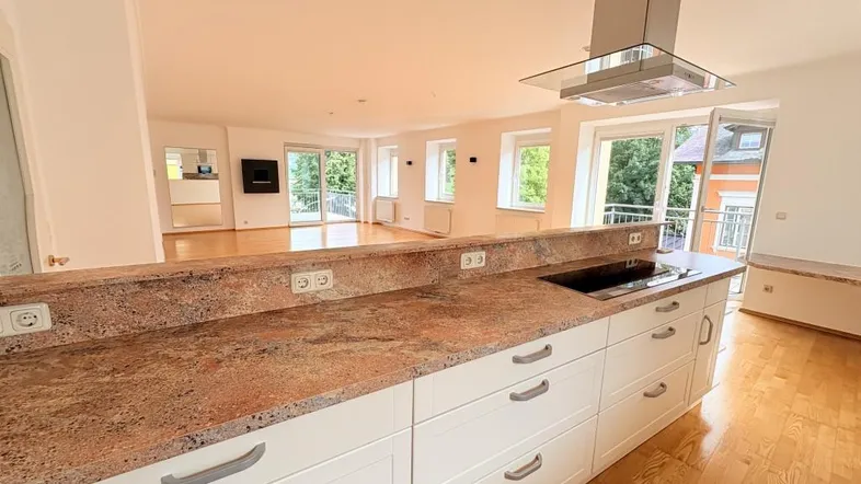 Moderne Küche mit Granitarbeitsplatte und offener Verbindung zum hellen Wohnbereich mit Holzboden.