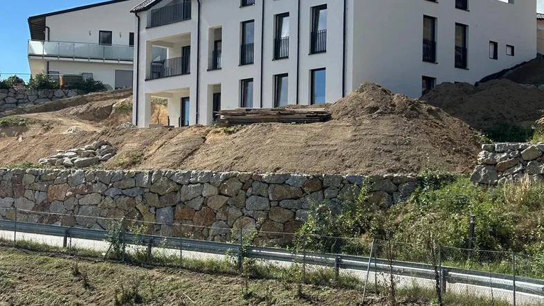 Modernes Mehrfamilienhaus im Bau mit weißer Fassade und Solarpaneelen auf dem Dach.
