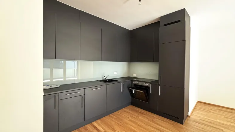 Moderne Einbauküche in Dunkelgrau mit integrierten Geräten und Holzfußboden.
