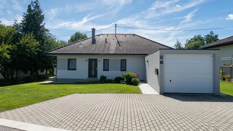 Modernes Einfamilienhaus mit gepflegtem Vorgarten, großer Auffahrt und integrierter Garage unter blauem Himmel.