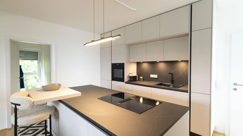Moderne Küche mit Kücheninsel, Induktionskochfeld und integrierten Geräten in hellen Farbtönen.