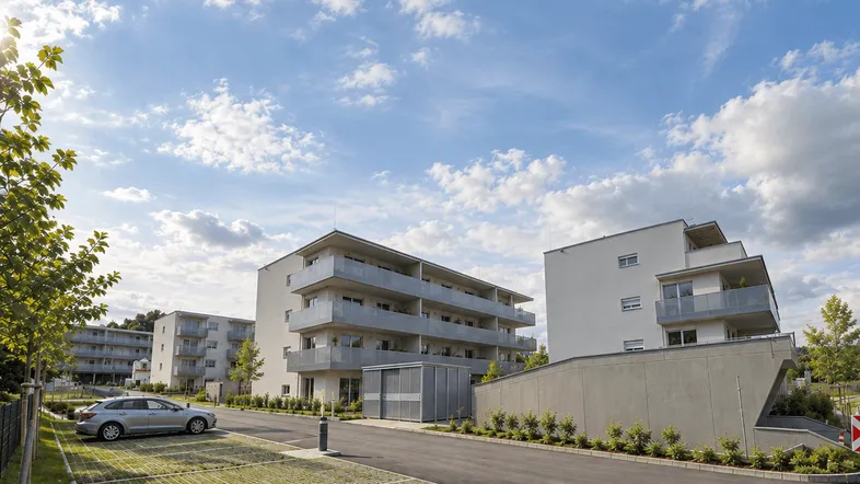 Moderne Mehrfamilienhäuser mit Balkonen, Außenparkplätzen und gepflegter Grünanlage unter blauem Himmel.