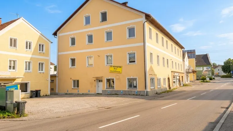 Gelbes Mehrfamilienhaus mit mehreren Stockwerken und einem "Zu vermieten"-Schild an einer Straße gelegen.