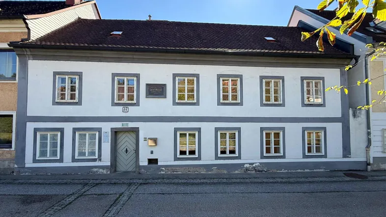 Historisches Gebäude mit weißer Fassade, grauen Akzenten und vielen Fenstern unter blauem Himmel.