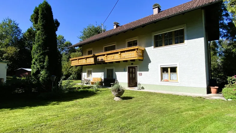 Hausfassade mit Holzbalkon und gepflegtem Vorgarten unter blauem Himmel.