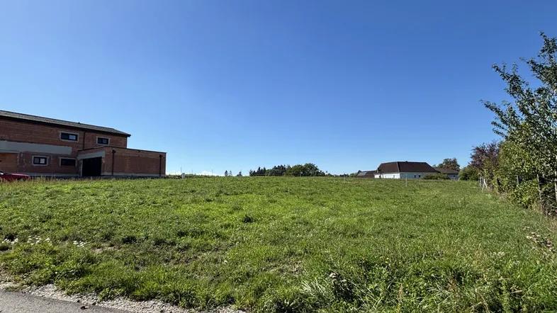 Weitläufiges grünes Grundstück unter blauem Himmel mit umliegenden Gebäuden in ländlicher Umgebung.