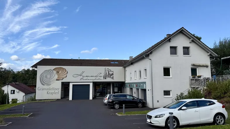 Außenansicht eines Geschäftsgebäudes mit Bäckerei-Beschilderung und Parkplätzen unter blauem Himmel.
