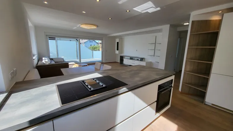 Heller, offener Wohn- und Essbereich mit moderner Küche, Holzboden und Zugang zum Balkon.