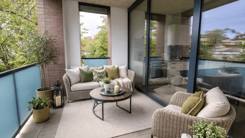Einladender Balkon mit bequemen Outdoor-Möbeln, Pflanzen und Blick ins Grüne sowie auf eine moderne Küche.