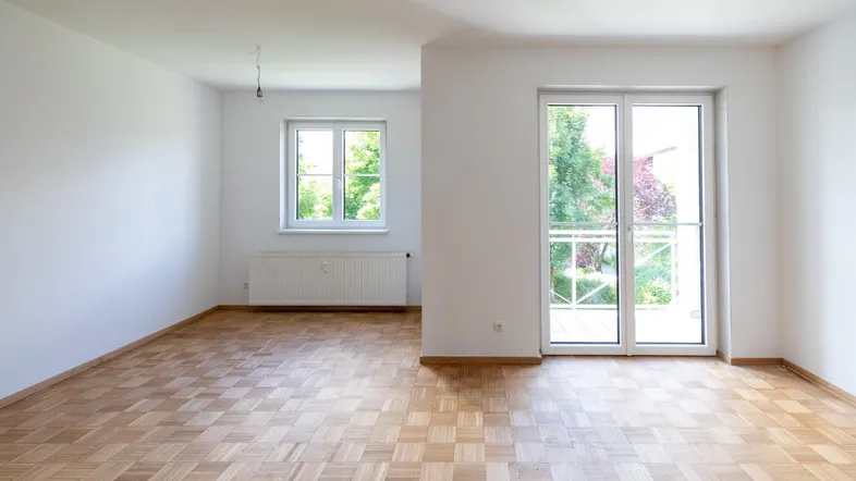 Helles, leeres Zimmer mit Parkettboden und Zugang zu einem französischen Balkon.