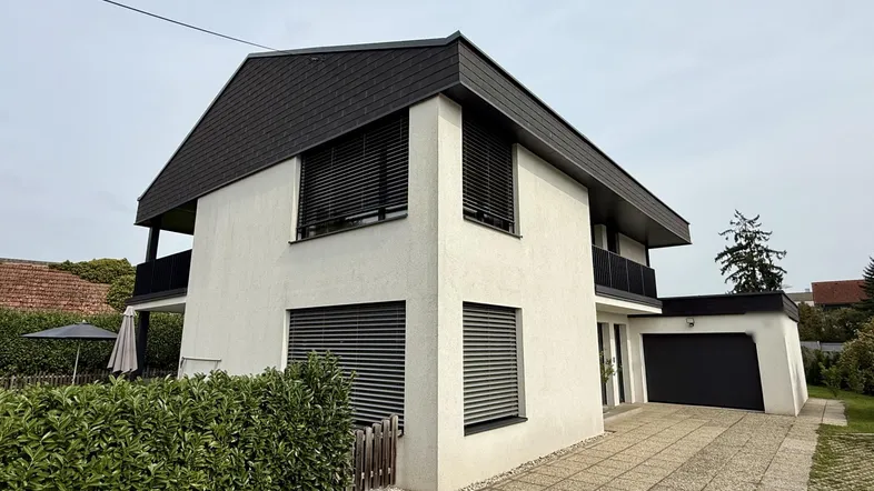 Modernes Einfamilienhaus mit weißer Fassade, schwarzem Dach und integrierter Garage.
