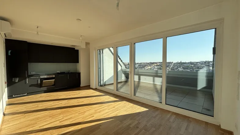 Heller offener Wohnbereich mit moderner Einbauküche, Holzboden und Zugang zu einer sonnigen Terrasse mit Stadtblick.