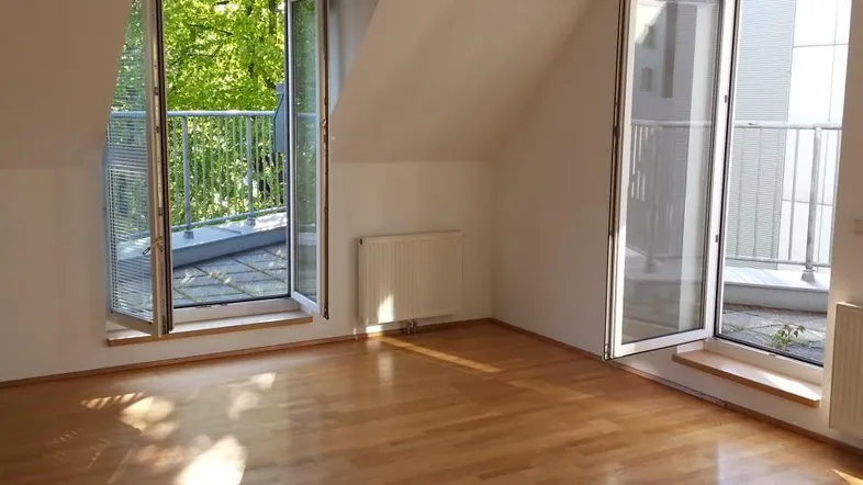 Helles Zimmer im Dachgeschoss mit Holzboden und Zugang zu zwei Balkonen, bietet viel natürliches Licht.