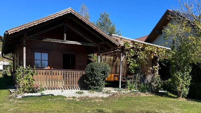 Rustikales Holzhaus mit überdachter Terrasse und gepflegtem Garten unter blauem Himmel.