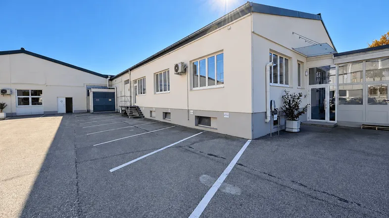 Großes Geschäftsgebäude mit Parkplätzen und sonnigem Wetter, ideal für gewerbliche Nutzung.