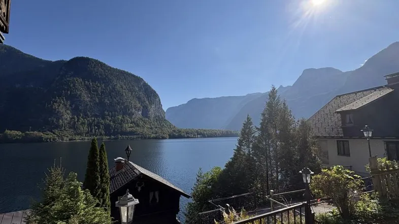 Sonniger Blick von einer Terrasse auf den See und die umliegenden Berge mit traditionellen Häusern.