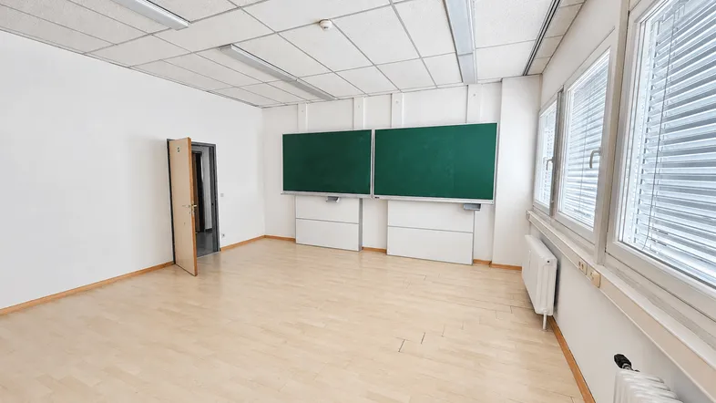 Heller, leerer Klassenraum mit zwei grünen Tafeln und großen Fenstern, ideal für Bildungszwecke.