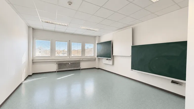 Leerer Klassenraum oder Büroraum mit großen Fenstern, Tafeln und einem Rasterdecken-System.
