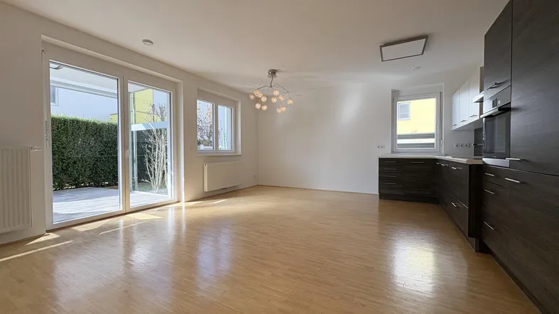 Heller Wohn-Essbereich mit integrierter Küche, Holzboden und Zugang zur Terrasse.