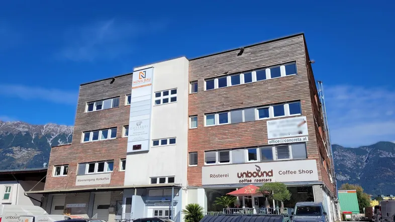 Mehrstöckiges Geschäftsgebäude mit Holzfassade und Büroräumen, umgeben von Bergen unter blauem Himmel.
