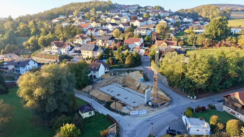 Luftaufnahme einer Baustelle in einer Wohnsiedlung mit vielen Häusern und grüner Umgebung.