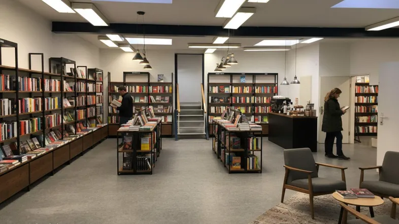 Geräumiger Verkaufsraum mit Bücherregalen, Sitzgelegenheiten und einem kleinen Cafébereich, gut beleuchtet durch Oberlichter.