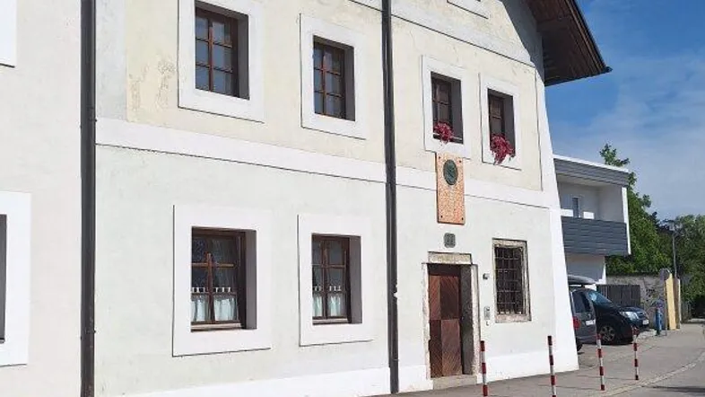 Traditionelles Gebäude mit heller Fassade, Holzdach und braunen Fenstern an einer Straße.