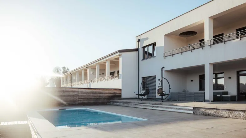 Moderne Architektur mit Außenpool und großzügiger Terrasse unter strahlendem Sonnenschein.