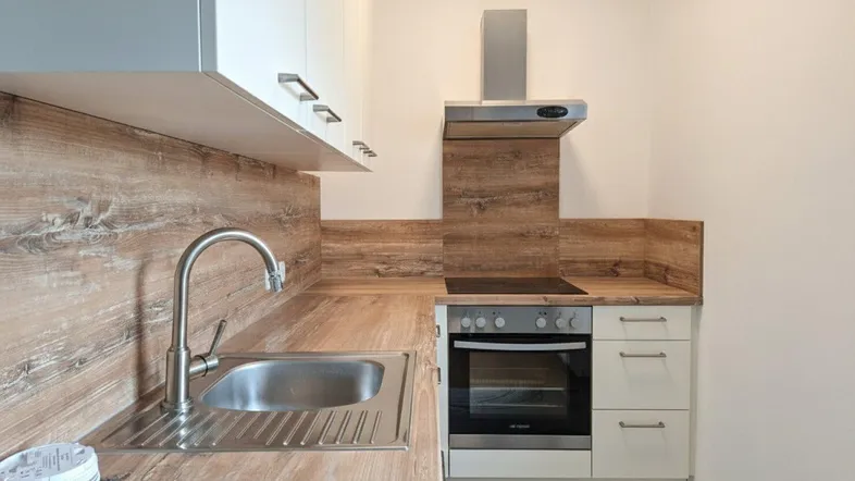 Kompakte Küche mit Holzdekor-Arbeitsplatte, weißen Schränken und integrierten Geräten.