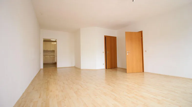 Heller, leerer Wohnbereich mit Laminatboden und weißen Wänden, der Zugang zu weiteren Räumen bietet.