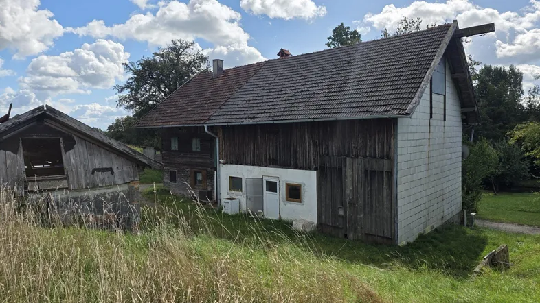 Altes Bauernhaus mit Holzelementen und Satteldach in ländlicher Umgebung, umgeben von Wiesen.