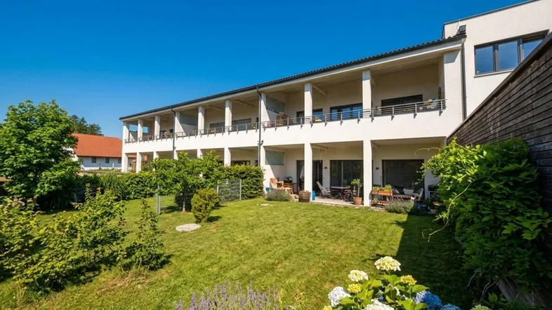 Moderne Wohnanlage mit gepflegtem Garten, Terrassen und Balkonen unter blauem Himmel.