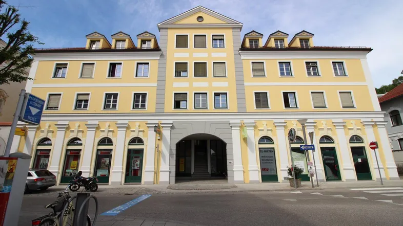 Gelbe Fassade eines modernen Gebäudes mit vielen Fenstern und Mansarddach in städtischer Umgebung.