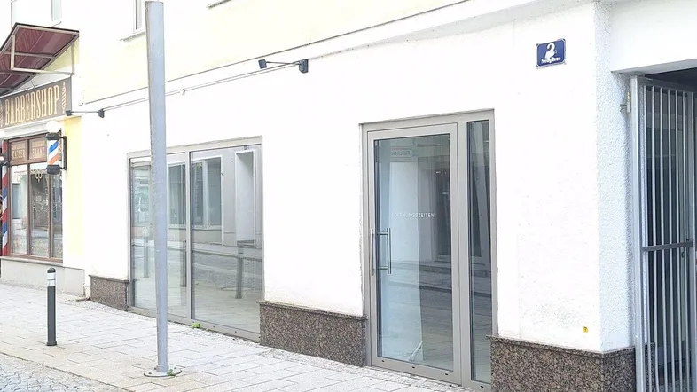 Vorderansicht eines modernen Geschäftsgebäudes mit großen Glasfenstern und Eingangstür zur Straße.