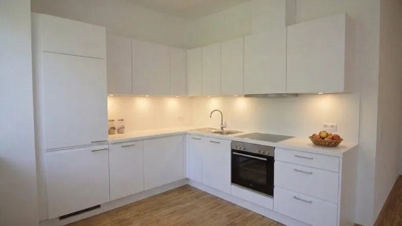 Moderne weiße Einbauküche mit Holzfußboden und integrierten Geräten in hellem Raum.