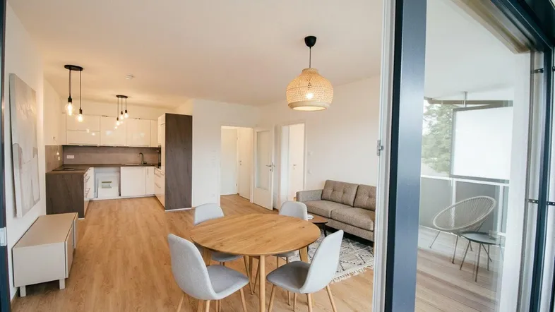 Heller offener Wohn-Essbereich mit integrierter Küche, Parkettboden und Zugang zum Balkon.