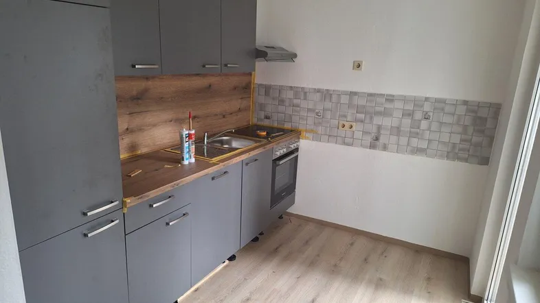 Moderne Küche mit grauen Schränken, Holzoptik-Arbeitsplatte und heller Laminatboden.