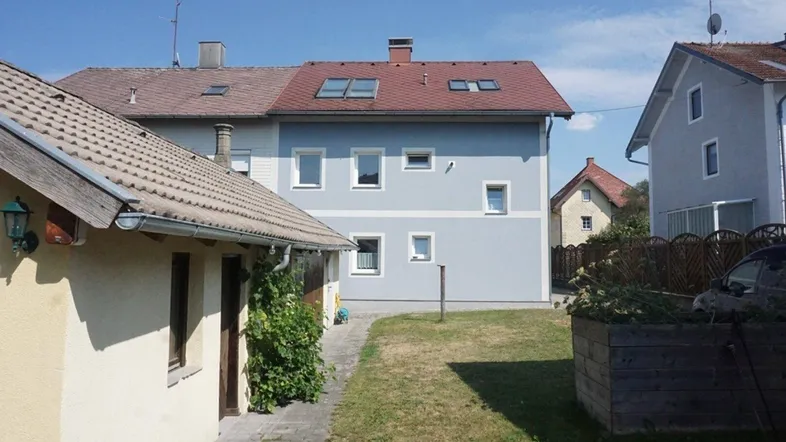 Rückansicht des Hauses mit hellblauer Fassade, roten Dachziegeln und einem kleinen Gartenbereich.