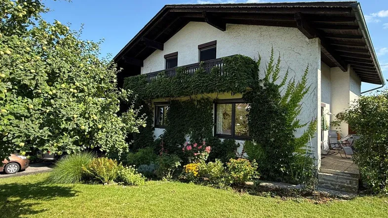 Traditionelles Haus mit begrüntem Balkon und gepflegtem Garten unter blauem Himmel.