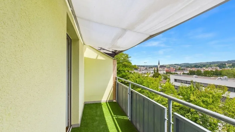 Heller Balkon mit Kunstrasen und weitem Blick über die Stadt und grüne Hügel.