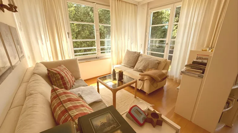 Helles Wohnzimmer mit bequemer Sitzecke, Parkettboden und großen Fenstern mit Blick ins Grüne.