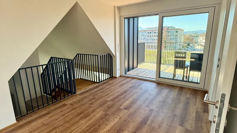 Heller Wohnbereich mit Holzboden, offener Treppe und Zugang zu einem sonnigen Balkon.