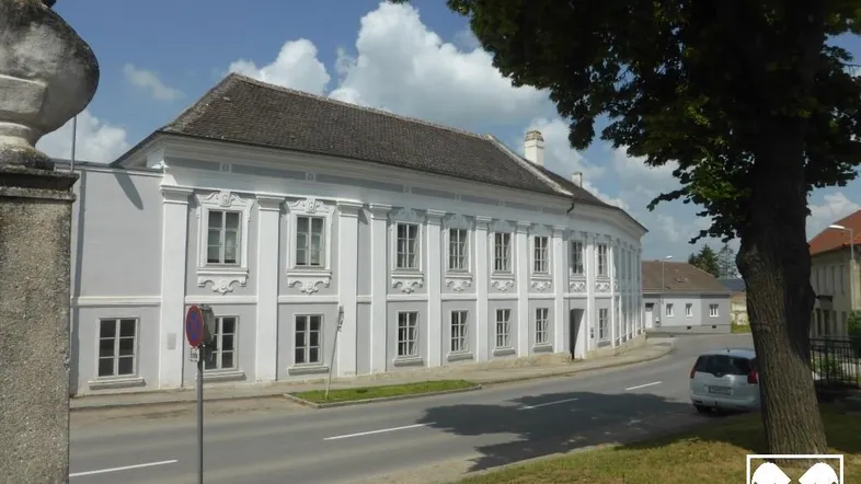 Historisches Gebäude mit klassischer Architektur und vielen Fenstern entlang einer sonnigen Straße.