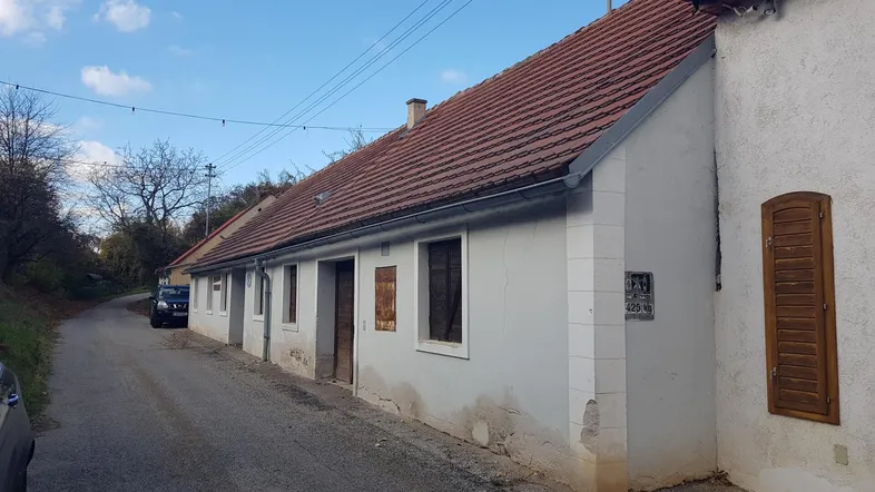 Ländliches Gebäude mit Ziegeldach und einfacher Fassade entlang einer unbefestigten Straße.