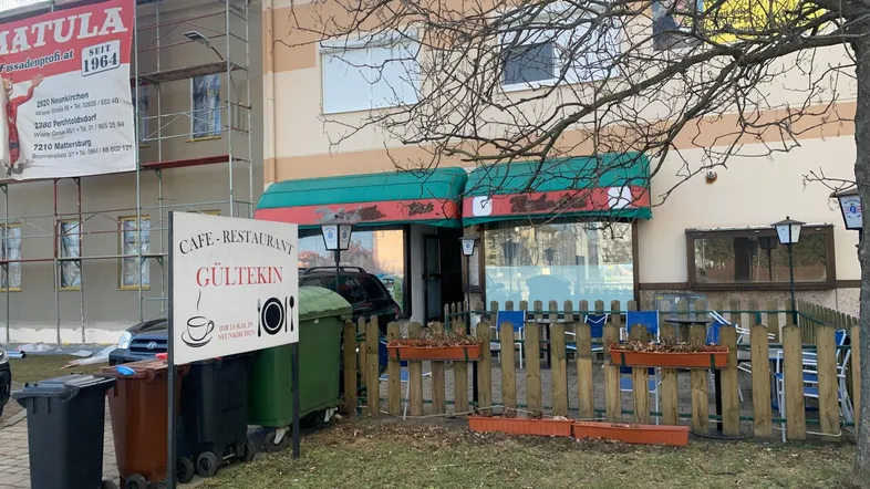 Außenansicht eines Gebäudes mit Café-Restaurant, Gerüst und provisorischem Außenbereich mit Tischen.