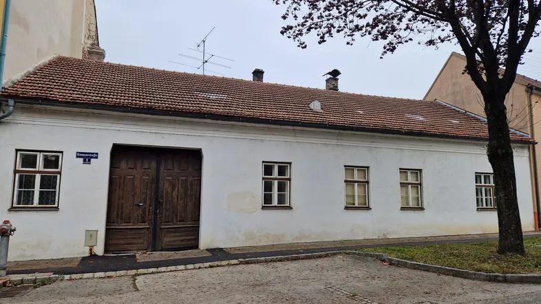 Altes Wohnhaus mit weißer Fassade, traditionellem Ziegeldach und großen Holztoren an einer ruhigen Straße.